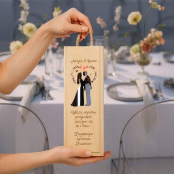 Osoba trzymająca skrzynkę na wino z motywem ślubnym na tle dekoracji weselnego stołu