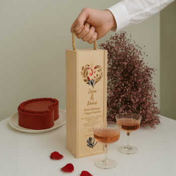 Skrzynka ślubna z humorem na tle różowego wina, ciasta i płatków róż