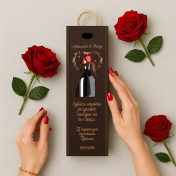 Brązowe pudełko na wino z motywem róż, obok rozłożone czerwone róże i kobiece dłonie z czerwonym lakierem