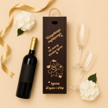 Eleganckie pudełko na wino z dedykacją i grafiką gołębi, ustawione na płaskim tle obok butelki wina, kieliszków i białego kwiatu.