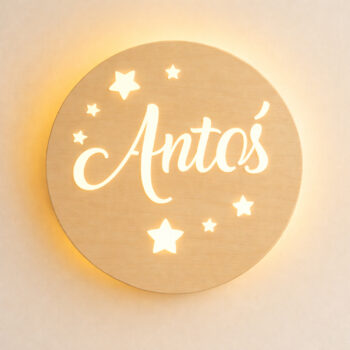 Zbliżenie świecącej, okrągłej lampki z imieniem „Antoś” i gwiazdkami na jasnej ścianie.