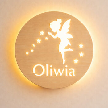 Zbliżenie świecącej lampki z wróżką, gwiazdkami i napisem „Oliwia” na jasnej ścianie.