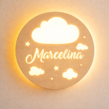 Zbliżenie świecącej lampki z chmurką, gwiazdkami i napisem „Marcelina” na jasnej ścianie.