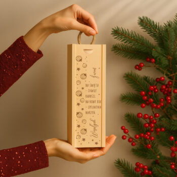 Drewniana skrzynka na wino z grawerem i bombkami w aranżacji z choinką i czerwonymi ozdobami.