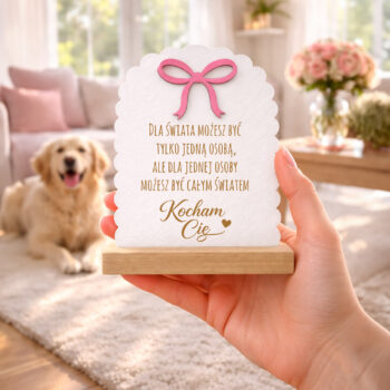 Statuetka z grawerem w bukowej podstawie – trzymana w dłoni w salonie, w tle pies i sofa.