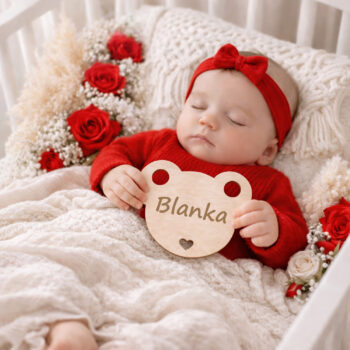 Noworodek w czerwonym stroju z drewnianą tabliczką z imieniem